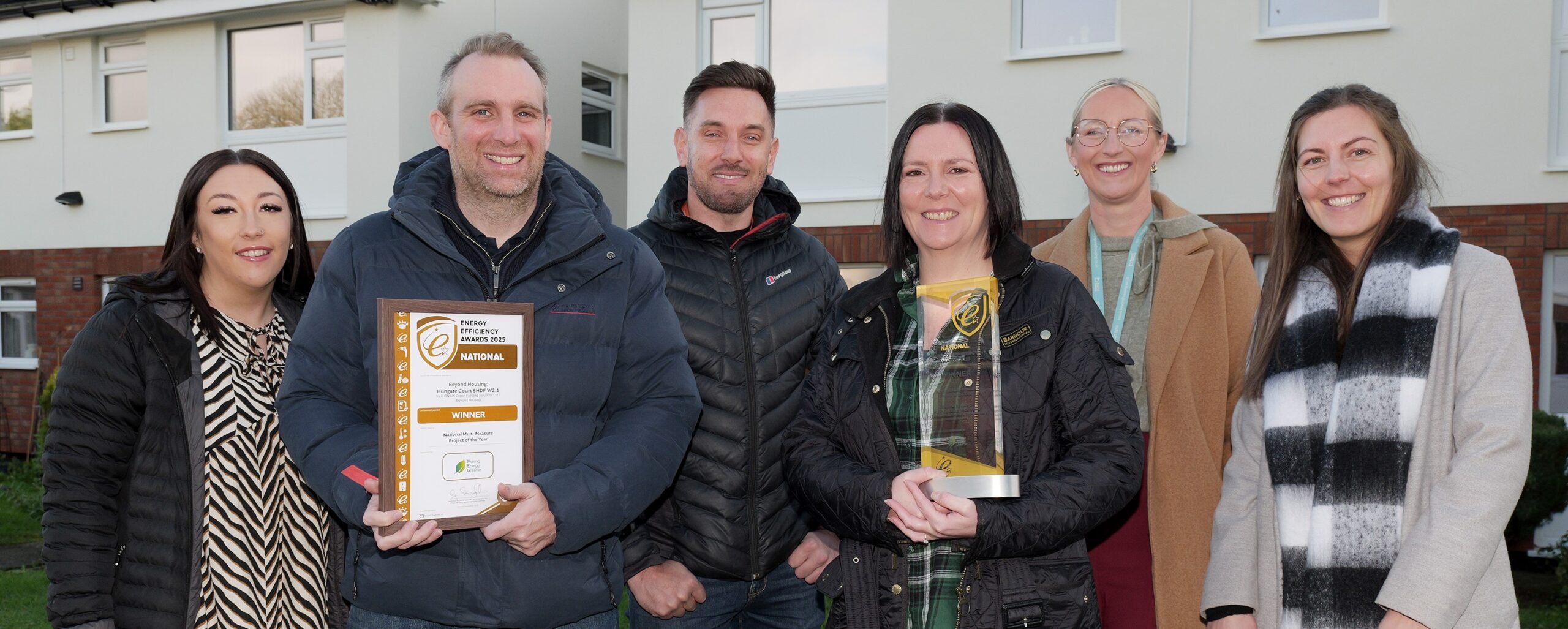6 people stood outside. 1 holding a glass award, and one holding a certificate