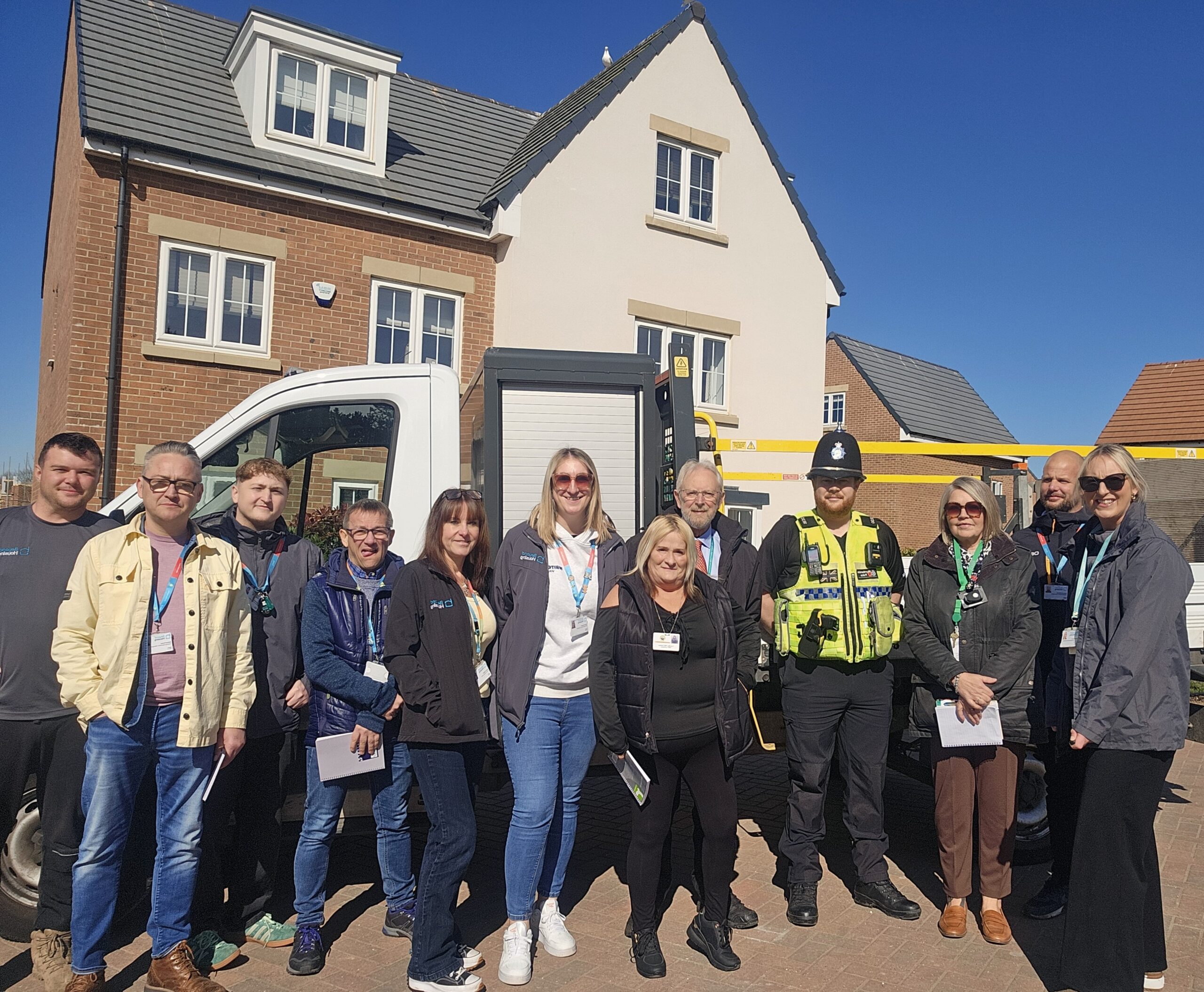 Twelve people stood in front of a van and a house