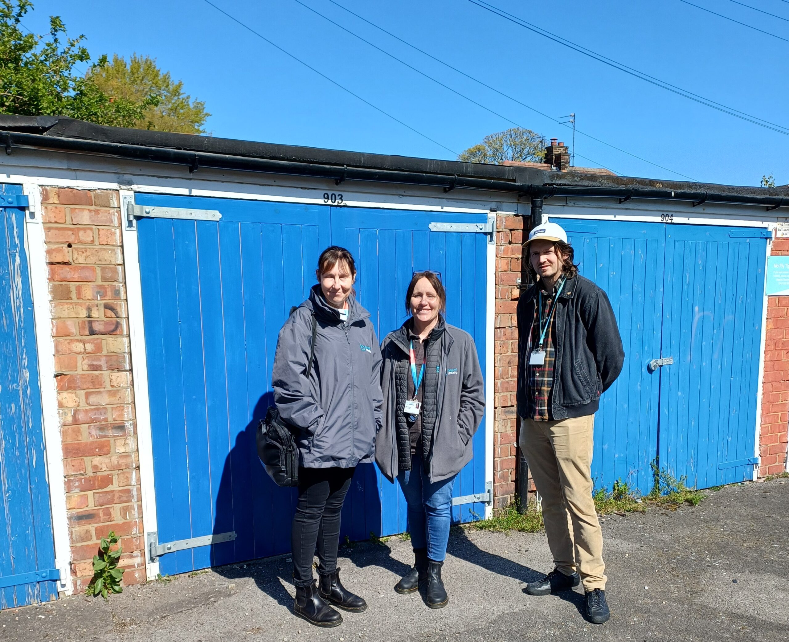 Three people stood in front of blue garages